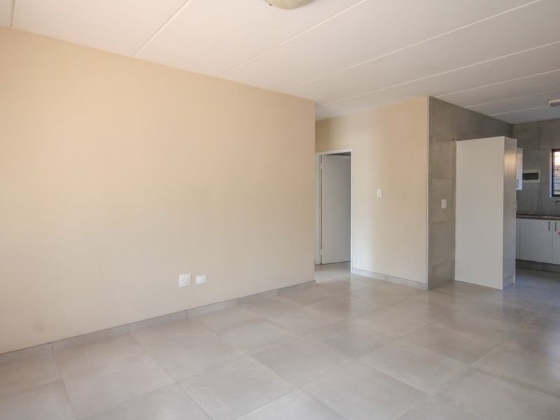 An open-plan living area featuring neutral tiled flooring and a connected kitchen space with built-in cabinetry and sink.