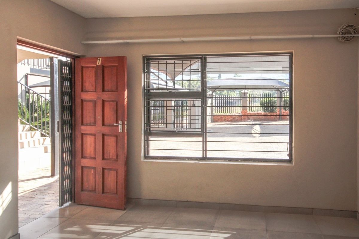An empty living area featuring tiled floors, a timber entrance door with a security gate, and a window fitted with security bars.