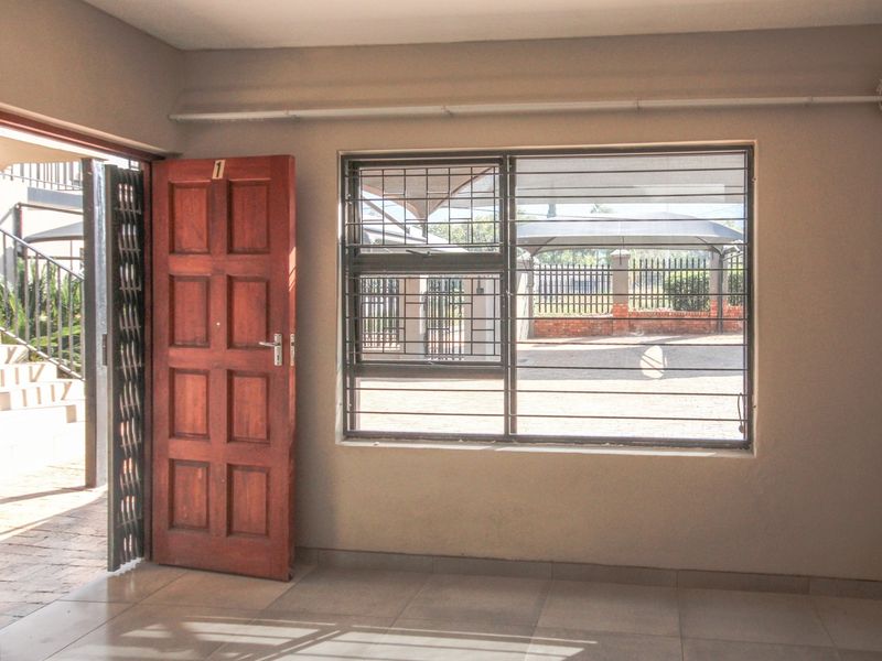 An empty living area featuring tiled floors, a timber entrance door with a security gate, and a window fitted with security bars.