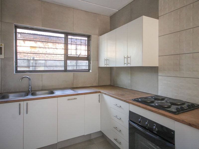 A clean, modern kitchen featuring white cabinetry, wood-look countertops, a built-in oven and hob, and neutral wall tiling.