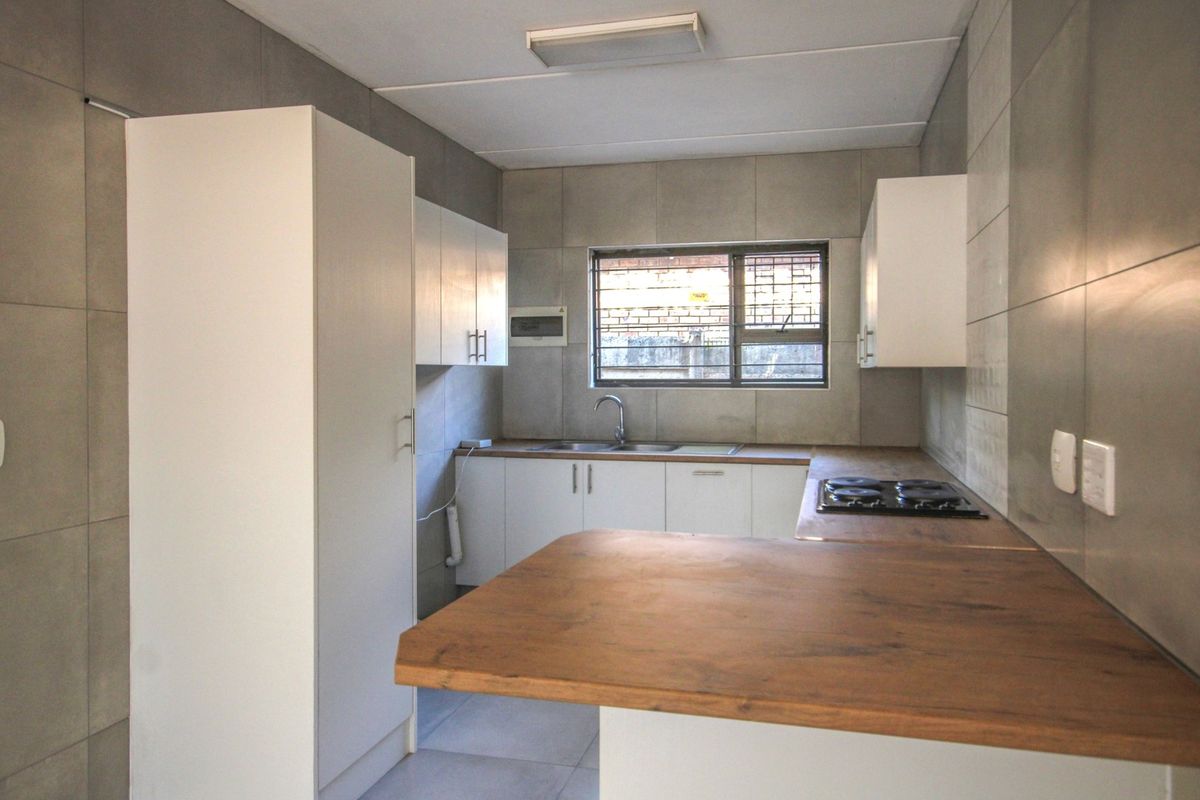 A clean, modern kitchen featuring white cabinetry, wood-look countertops, a built-in hob, and neutral grey wall tiling.