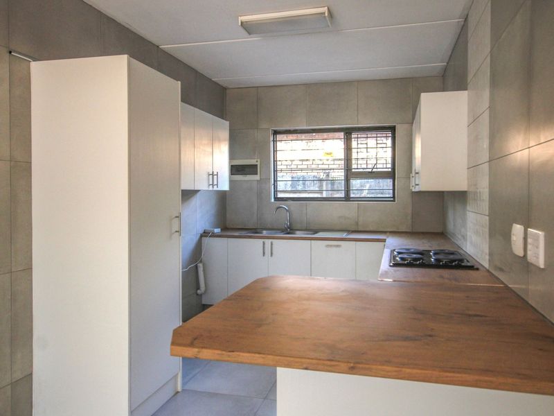 A clean, modern kitchen featuring white cabinetry, wood-look countertops, a built-in hob, and neutral grey wall tiling.