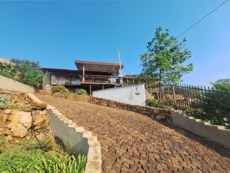 Front view of the property featuring a cobblestone driveway, stone retaining walls, and an elevated timber deck with a covered patio area.