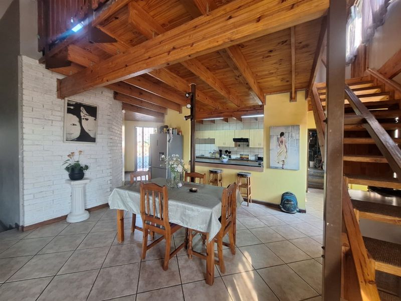 Open-plan living and dining area featuring exposed timber ceiling beams, a brick feature wall, and a functional kitchen with a breakfast counter.