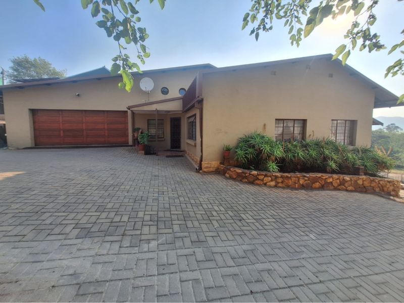 Front elevation of a house featuring a paved driveway, wooden garage door, and a stone retaining wall with established garden beds.