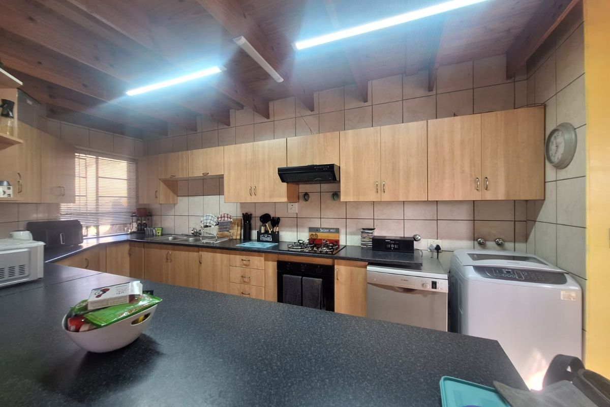 Functional kitchen featuring laminate cabinetry, dark countertops, gas hob, built-in oven, and exposed timber beam ceiling with tiled splashbacks.