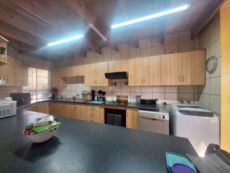 Functional kitchen featuring laminate cabinetry, dark countertops, gas hob, built-in oven, and exposed timber beam ceiling with tiled splashbacks.