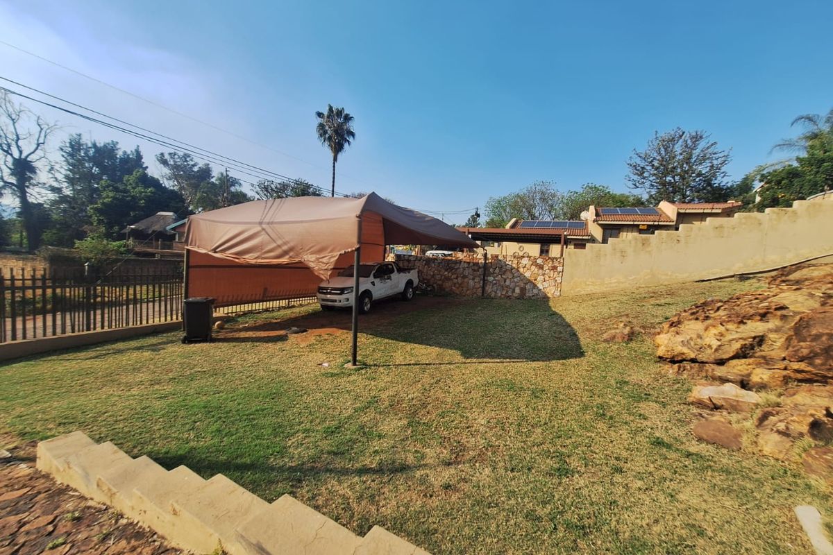 Rear garden area featuring a stone retaining wall, concrete steps, and a shaded parking structure.