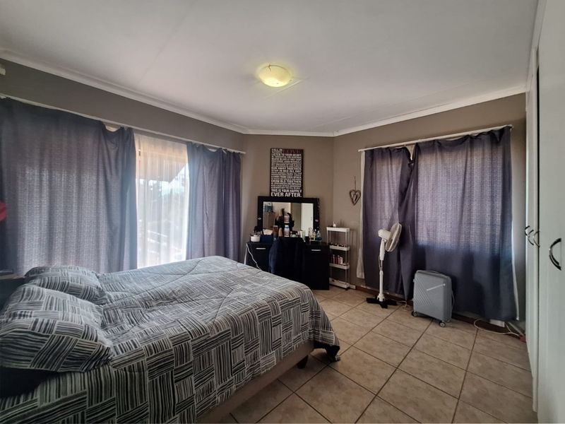 A spacious bedroom featuring tiled flooring, built-in cupboards, and dual window treatments, offering a functional and comfortable living space.