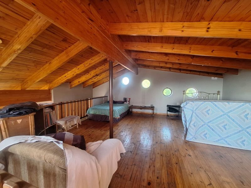Spacious loft-style bedroom featuring exposed timber rafters, vaulted wood ceilings, polished timber flooring, and unique circular porthole windows.
