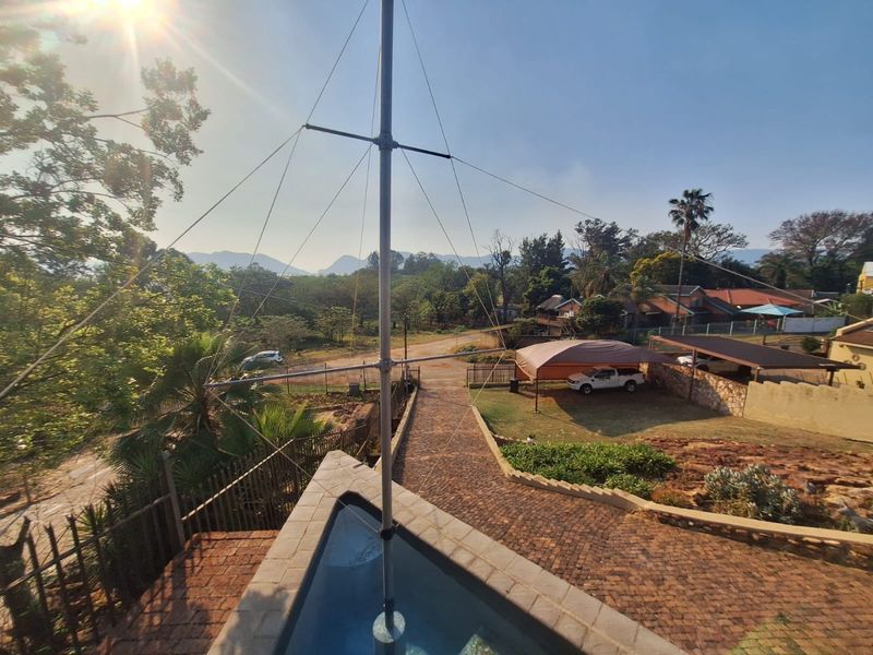Elevated view overlooking the property grounds, featuring a paved driveway, landscaped garden areas, and surrounding mountain scenery.