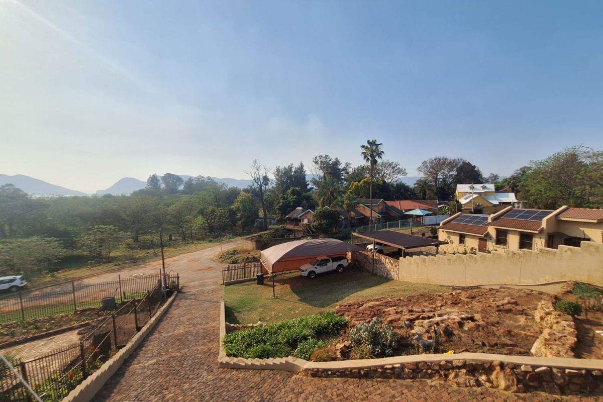 An elevated view of the property grounds featuring a paved driveway, retaining walls, solar panels on the roof, and a carport structure.