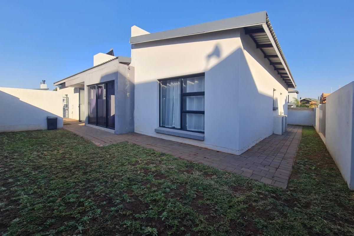 Rear view of the house featuring a paved patio area, sliding glass doors, and a surrounding boundary wall with a lawn.