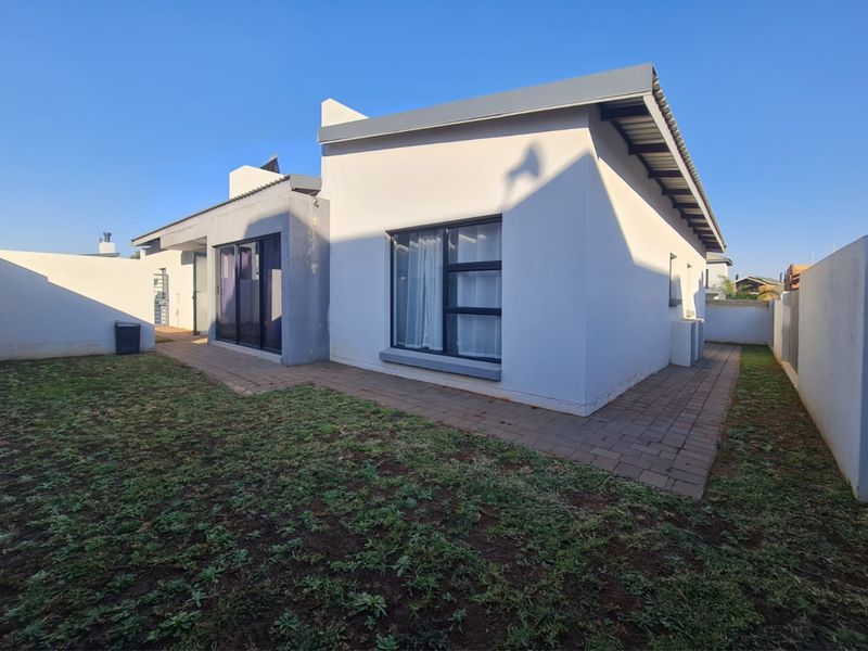 Rear view of the house featuring a paved patio area, sliding glass doors, and a surrounding boundary wall with a lawn.