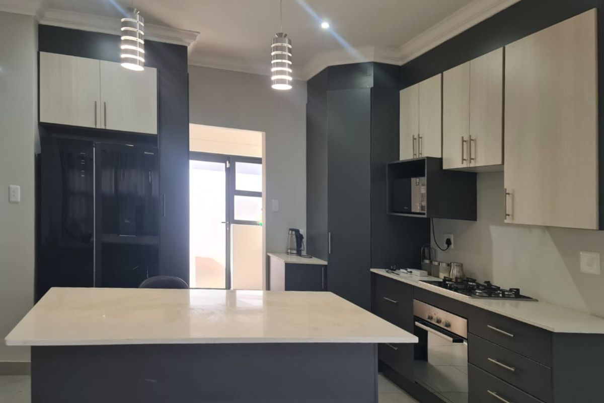 Modern kitchen featuring two-tone cabinetry, stone countertops, a central island, and integrated appliances including a gas hob and built-in oven.