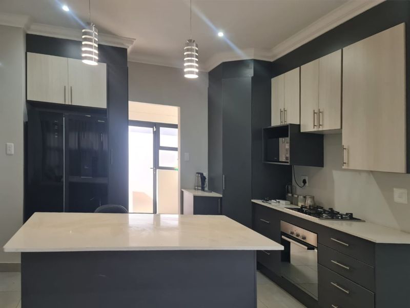 Modern kitchen featuring two-tone cabinetry, stone countertops, a central island, and integrated appliances including a gas hob and built-in oven.