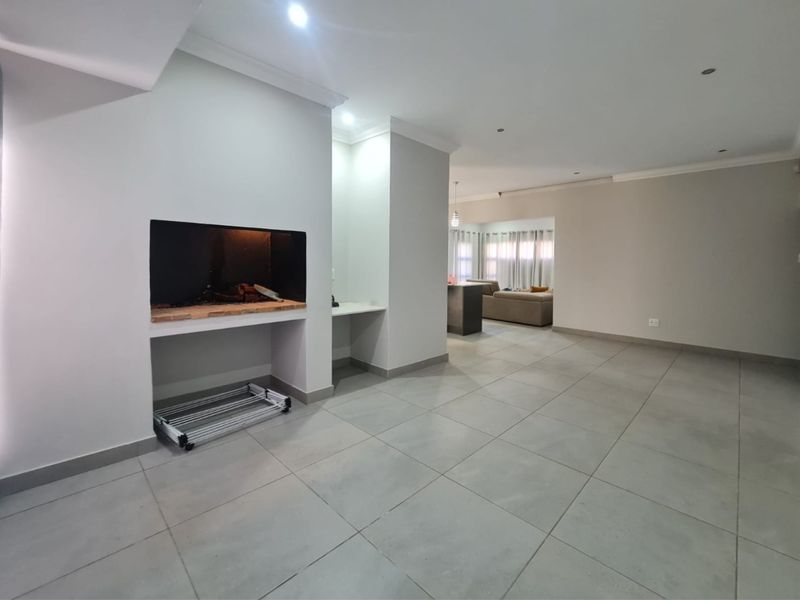 Spacious open-plan living area featuring large format floor tiles, a built-in fireplace, and recessed lighting, offering a clean and modern blank canvas.