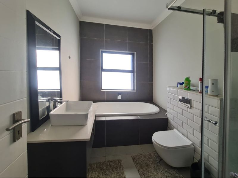 Modern bathroom featuring a vessel sink vanity, built-in bathtub with dark tiling, wall-mounted toilet, and a glass-enclosed shower area.