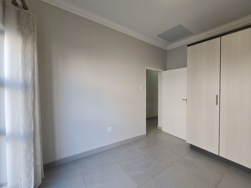 A clean, neutral bedroom featuring tiled flooring, built-in cupboards, and a ceiling access hatch, offering a blank canvas for personalization.