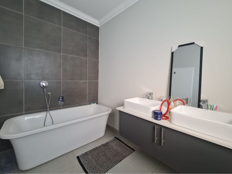 Modern bathroom featuring a sleek freestanding bathtub, a double vanity with vessel sinks, and contemporary dark grey wall tiling.