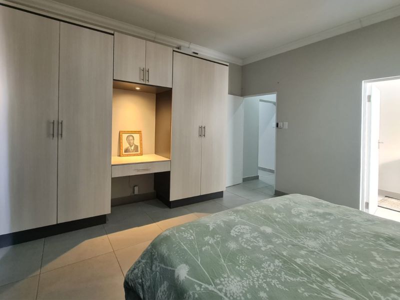 A well-maintained bedroom featuring extensive built-in cabinetry with an integrated vanity, neutral tiled flooring, and clean finishes.