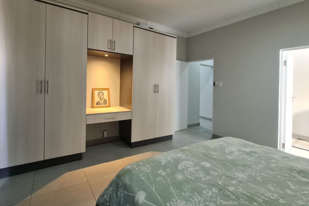A well-maintained bedroom featuring extensive built-in cabinetry with an integrated vanity, neutral tiled flooring, and clean finishes.
