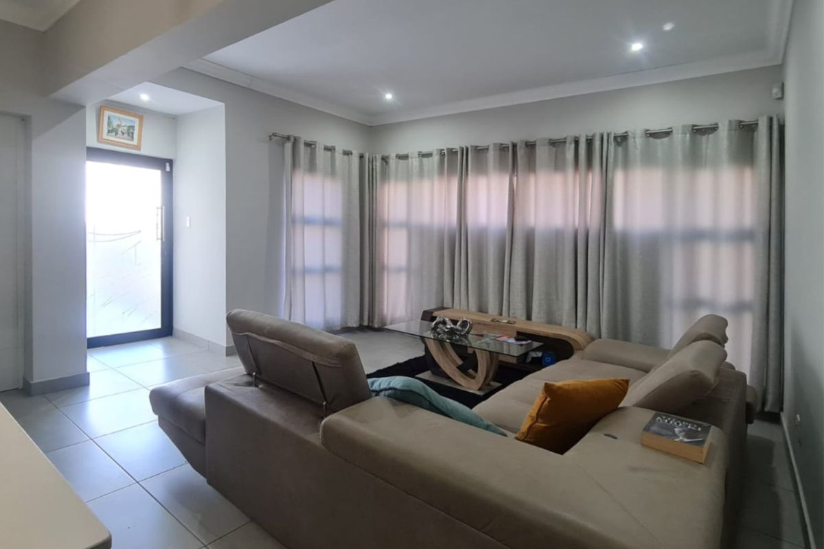 A well-lit living room featuring neutral tiled flooring, recessed ceiling lighting, and a sliding glass door providing access to the exterior.
