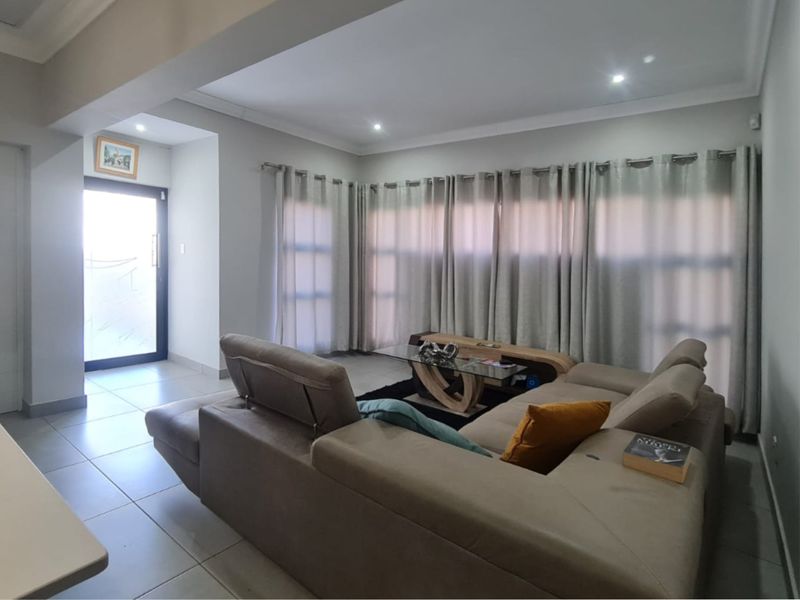 A well-lit living room featuring neutral tiled flooring, recessed ceiling lighting, and a sliding glass door providing access to the exterior.
