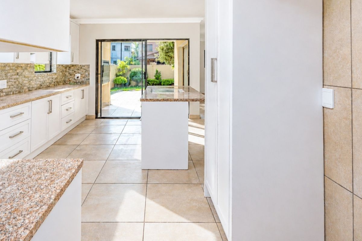 Modern kitchen featuring white cabinetry, granite countertops, tiled flooring, and a central island, with direct access to the rear patio through sliding glass doors.