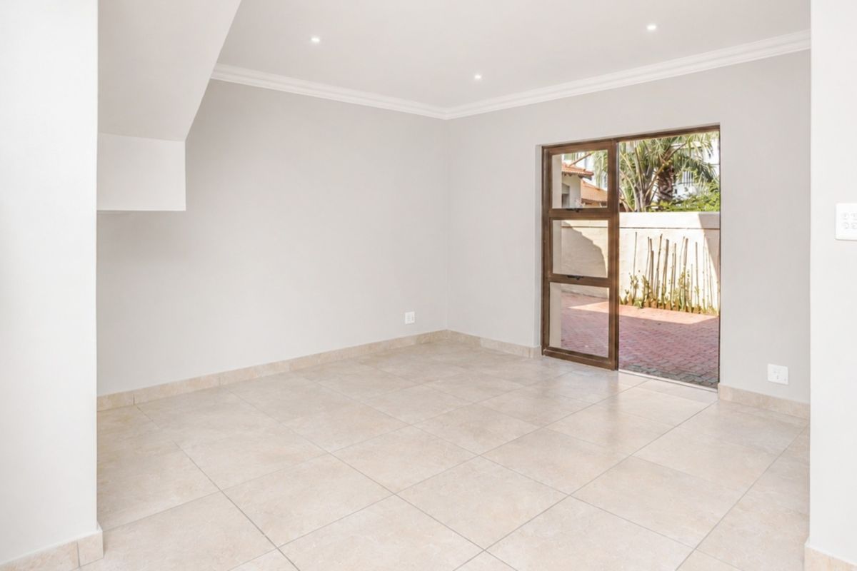 A bright, empty living area featuring neutral tiled flooring, recessed ceiling lighting, and a sliding glass door providing direct access to an outdoor patio.