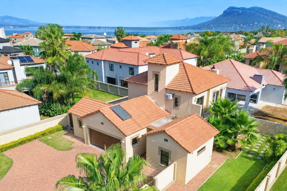 Aerial view of a residential property featuring a tiled roof, paved driveway, and landscaped garden, set within a scenic estate with mountain and water views.