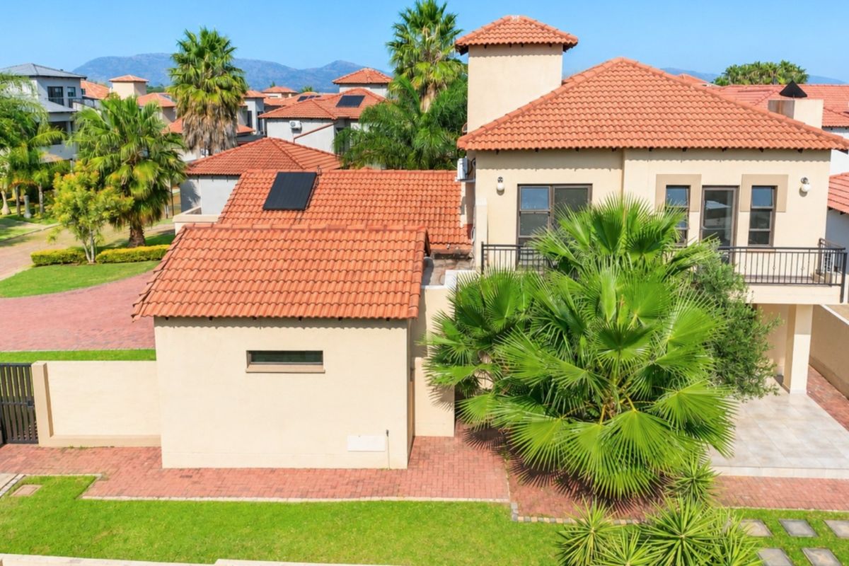 An elevated view of the rear exterior of a two-story house featuring a tiled roof, solar panels, a paved patio area, and a private garden.