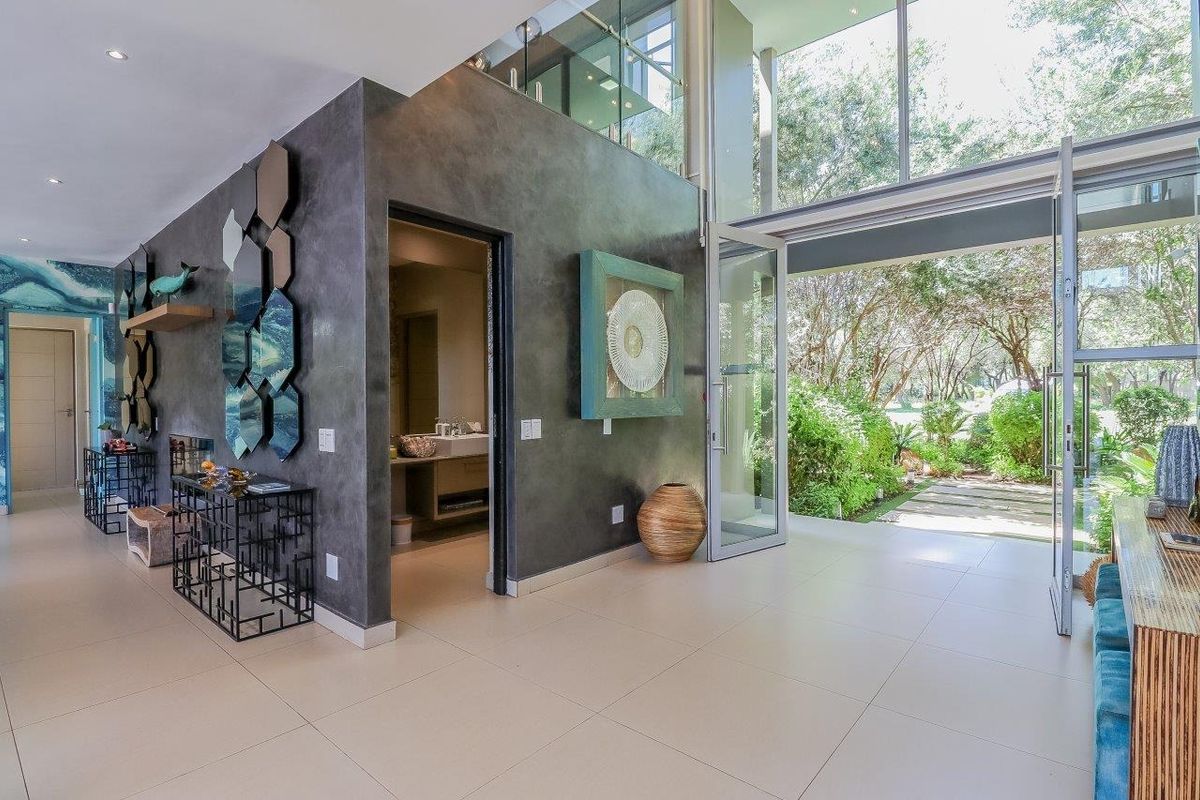 Modern living area featuring double volume ceilings, large format floor tiles, and expansive glass doors opening to a lush garden view.