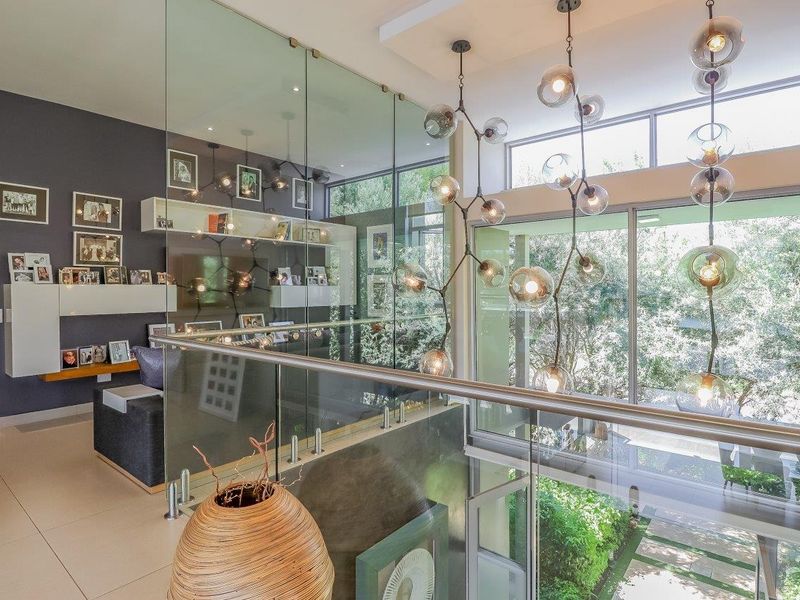 Modern living area featuring a glass balustrade, expansive windows with garden views, and contemporary built-in shelving with elegant pendant lighting.