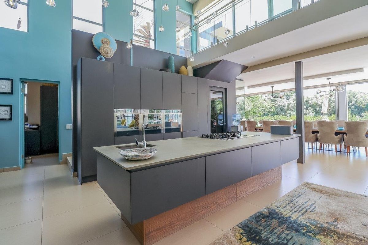 Modern open-plan kitchen featuring a large central island with gas hob, sleek dark cabinetry, and double-volume ceilings with contemporary pendant lighting.