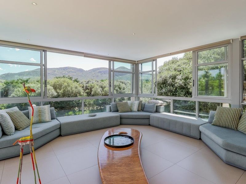 A bright, modern living room featuring expansive wrap-around windows that offer panoramic mountain views and abundant natural light.