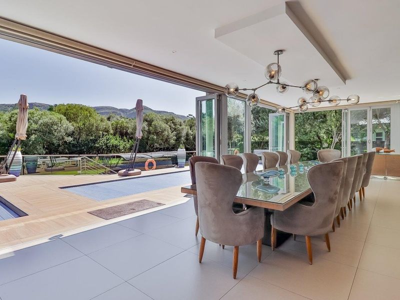 Spacious open-plan dining area featuring seamless indoor-outdoor flow through large bi-fold doors leading to a timber deck and swimming pool.
