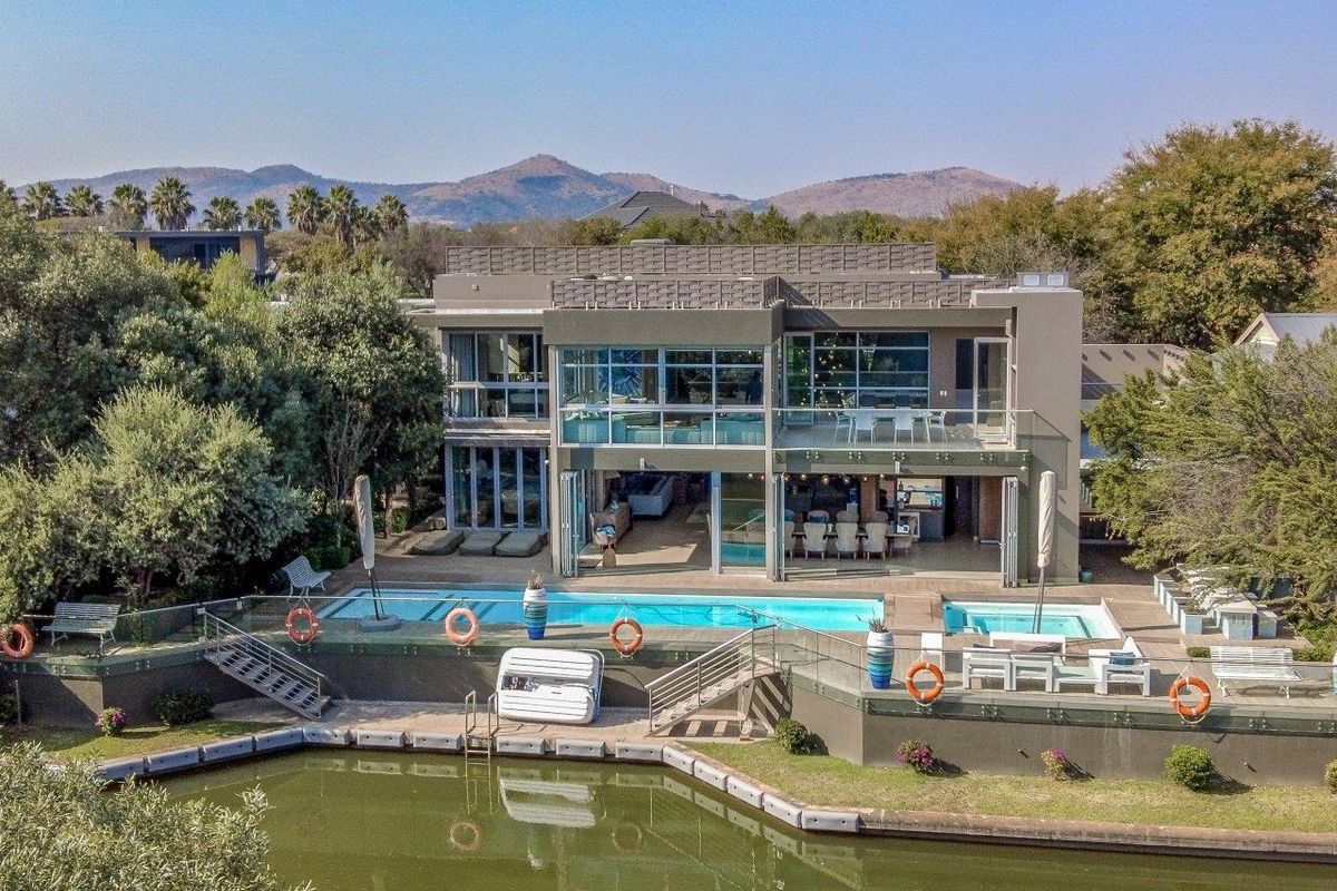 Aerial view of a modern multi-level residence featuring a swimming pool, spa, expansive rear patio, and direct water frontage with mountain views.