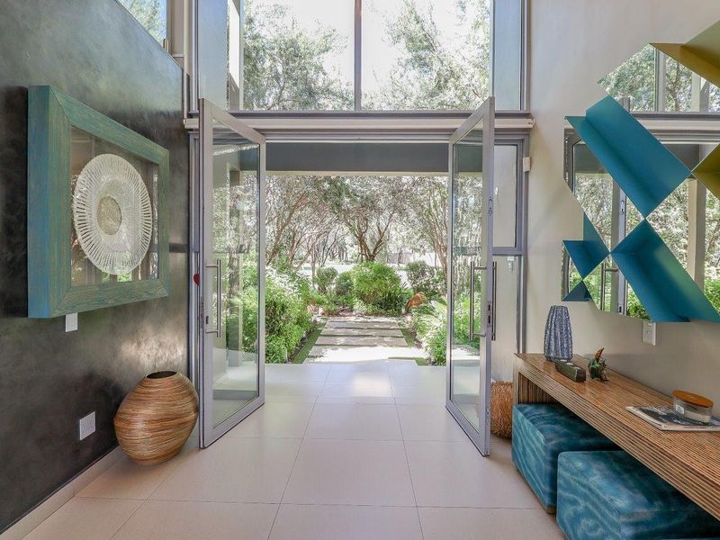 A bright and modern entrance hall featuring double glass doors, floor-to-ceiling windows, and elegant tiled flooring, offering a seamless transition to the garden.