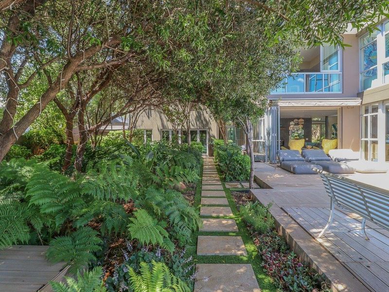 A lush, landscaped garden featuring a stone paver pathway leading to a timber deck and bi-fold doors opening into the home.