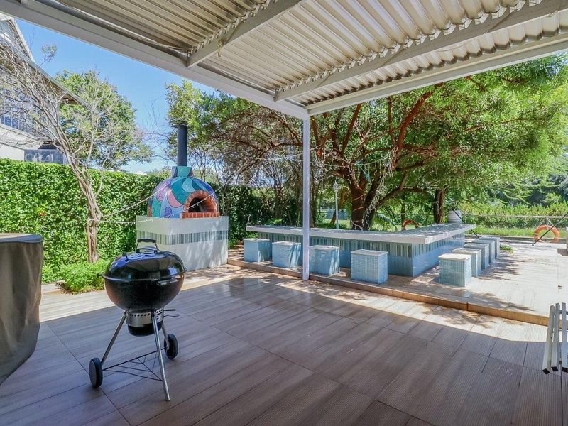 Covered outdoor patio featuring a built-in pizza oven, tiled bar counter, and durable flooring, perfect for alfresco dining and entertaining in a garden setting.