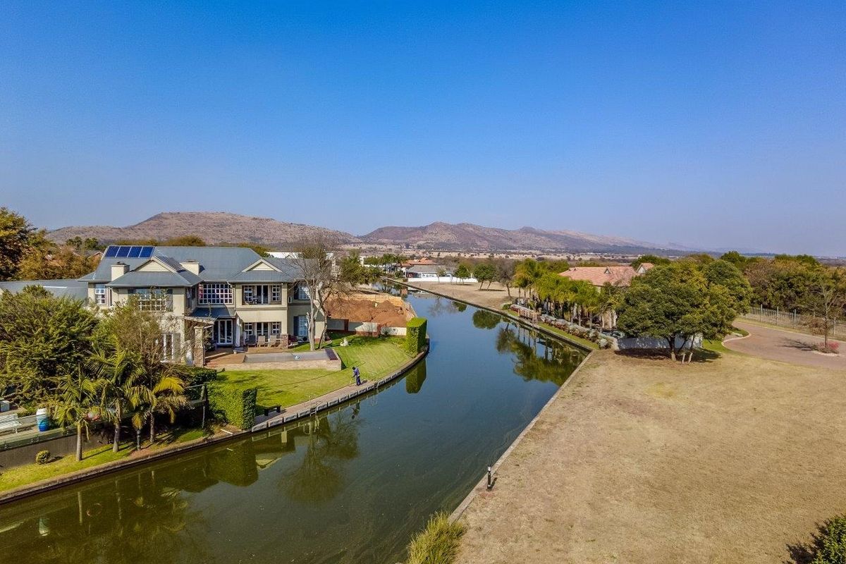 Aerial view of a large residential property situated along a canal, featuring a multi-story house with solar panels and landscaped garden areas.