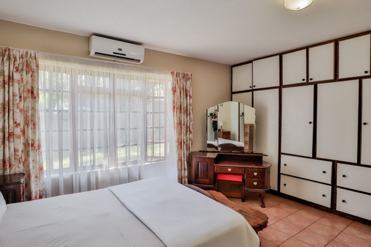 A bedroom featuring built-in floor-to-ceiling wardrobes, tiled flooring, and a wall-mounted air conditioning unit.