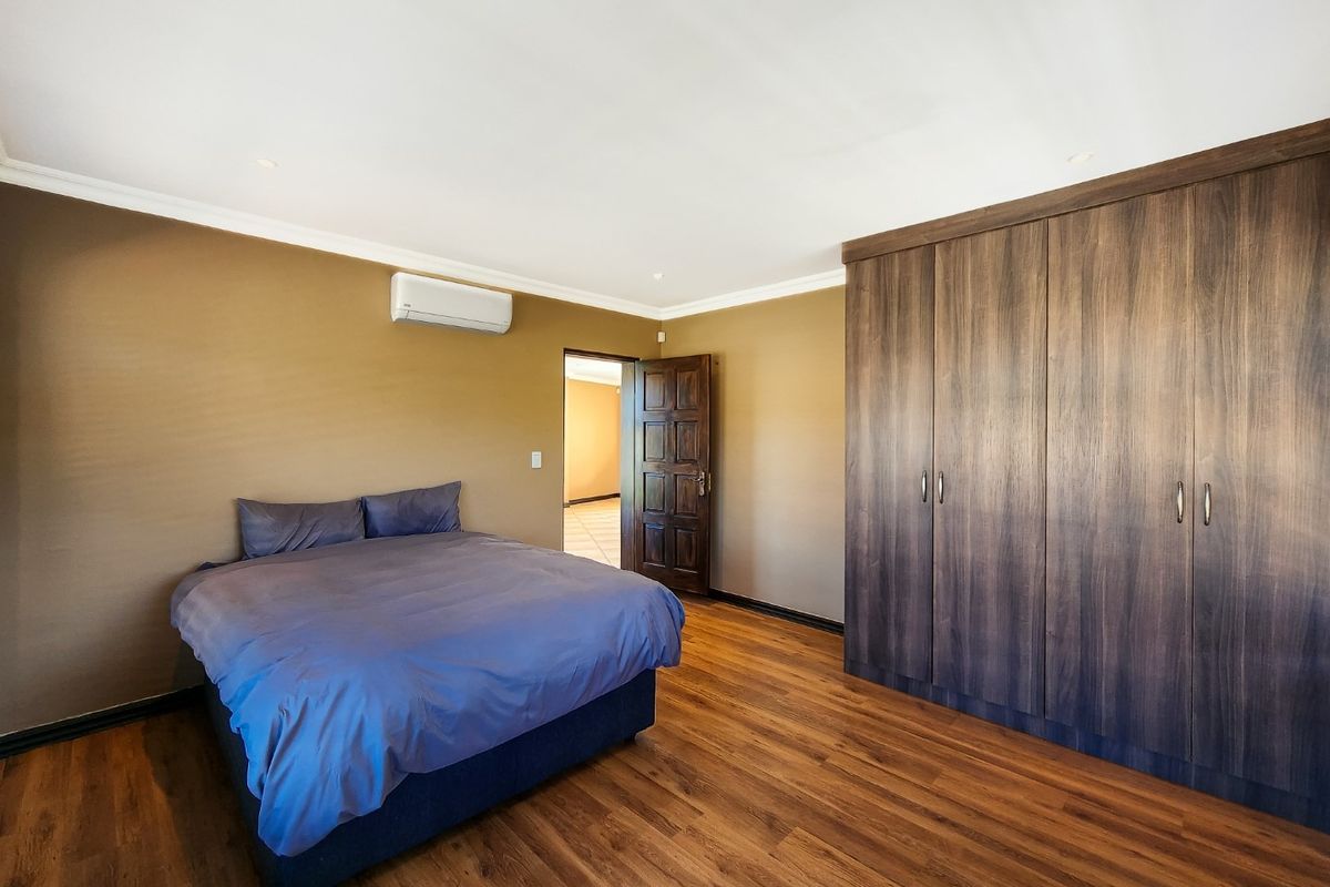 Spacious bedroom featuring warm-toned walls, dark wood-look flooring, built-in floor-to-ceiling cabinetry, and a wall-mounted air conditioning unit.
