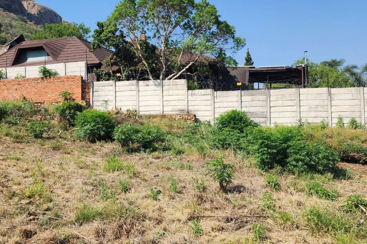 A view of a vacant residential plot featuring a sloped landscape, perimeter concrete walling, and electric fencing.