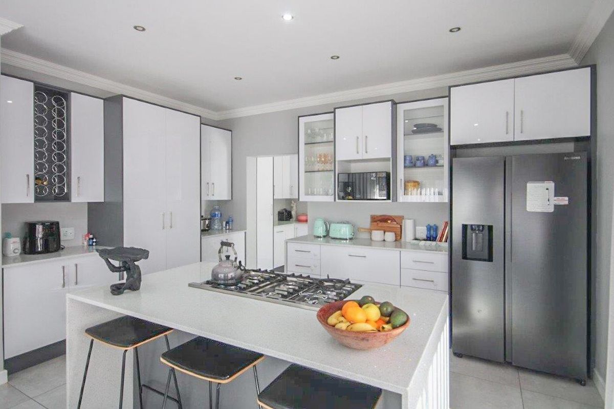 Modern kitchen featuring a central island with a built-in gas hob, sleek white cabinetry, stone countertops, and integrated storage solutions.