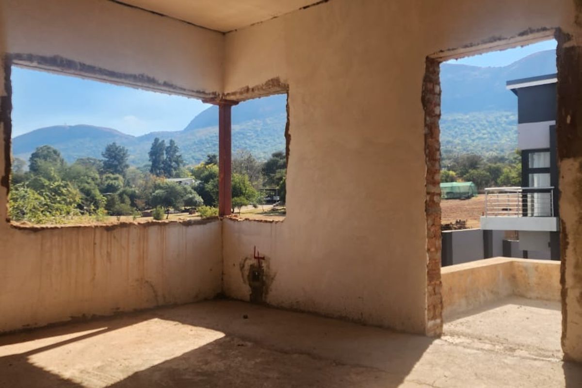 An unfinished interior room featuring exposed brickwork, raw plaster walls, and open window and door frames with scenic mountain views.