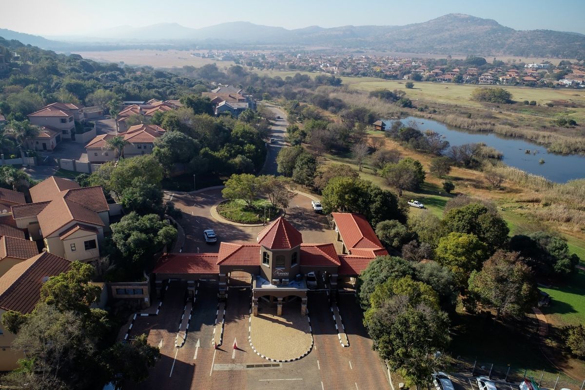 Aerial view of the secure estate entrance gatehouse, featuring paved access lanes, landscaped surroundings, and proximity to natural wetlands and residential properties.