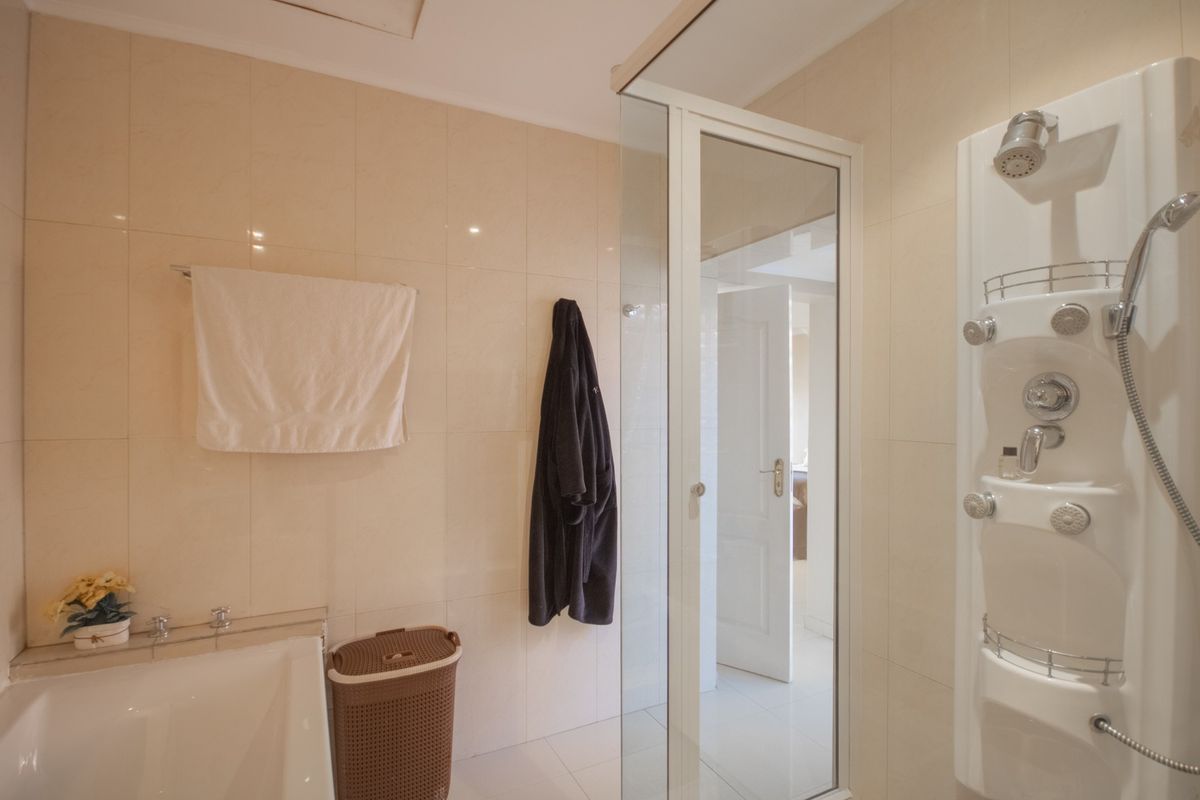 A functional bathroom featuring a built-in bathtub, a separate glass-enclosed shower stall with integrated shower panel, and neutral wall tiling.