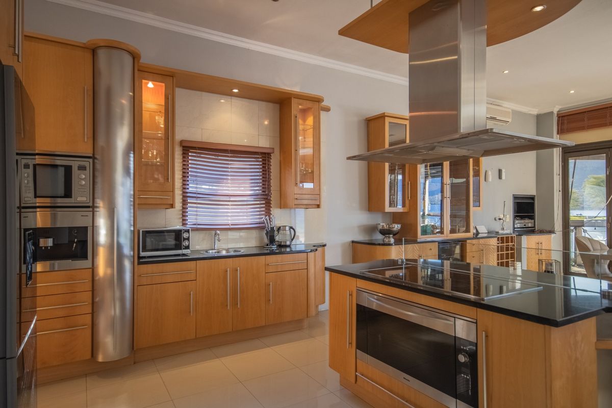 Modern kitchen featuring light wood cabinetry, black granite countertops, a central island with a built-in oven and hob, and a stainless steel extractor fan.